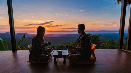 Wall Mural - a couple of men and women on vacation in Northern Thailand , staying at a homestay cabin hut in the mountains of Chiang Rai Doi Chang drinking tea on the wooden balcony at sunrise