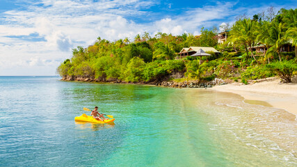 young men in a kayak on a tropical island in the Caribbean Sea, St Lucia or Saint Lucia. young man on vacation on a tropical island paddling in front of the beach with turqouse colored ocean