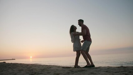 Canvas Print - Beautiful couple dancing on sea beach at sunset, low angle view. Slow motion effect