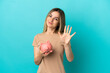 © luismolinero - Young woman holding a piggybank over isolated blue background counting five with fingers
