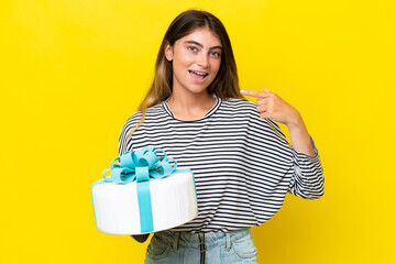 Wall Mural - Young caucasian woman holding birthday cake isolated on yellow background giving a thumbs up gesture