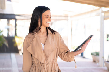 Wall Mural - Young woman at outdoors holding a tablet at outdoors with happy expression