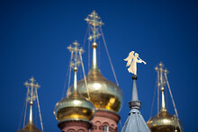 Gilded Angel Shaped Weathervane On The Steeple, Blurred Golden Domes And Crosses And Blue Sky On Background; Chernigovsky Skit, Sergiev Posad, Russia.