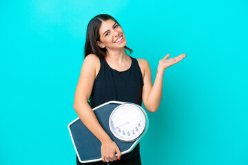 Wall Mural - Young Italian woman isolated on blue background with weighing machine