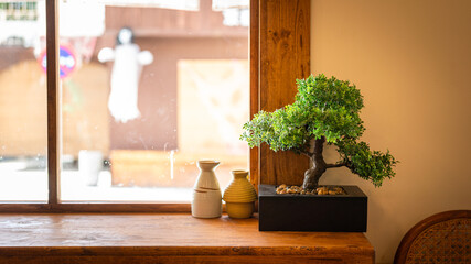 Wall Mural - Ceramic stonewares and bonsai tree are placed on the wooden table closed to the house window with day light outside. There are for Japanese style home decoration. Interior furniture object photo.