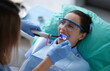 © H_Ko - Young woman dentist in protective gloves checking dental seal, fixing photopolymer lamp during stomatology procedure. Dentist specialist visiting patient in dental clinic.