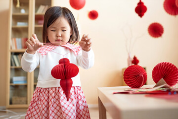 Wall Mural - Cute Asian little girl playing with red paper lanterns and decorations for Chinese New Year celebration at home, copy space