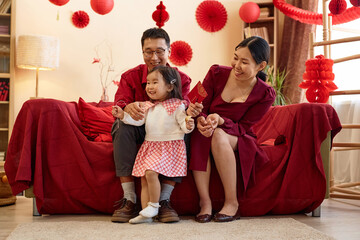 Wall Mural - Full length portrait of happy Asian family with little girl celebrating Chinese New year together at home all wearing red, copy space