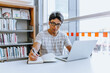 © Austockphoto - Man with glasses writing in notebook while using laptop in the library