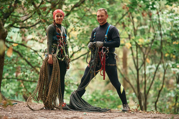 Wall Mural - Standing and posing. Man and woman doing climbing in forest with use of safety equipment