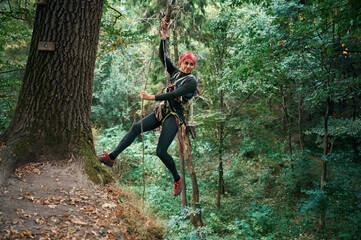 Wall Mural - Looking to the side, hanging on the rope. Woman is doing climbing in the forest by the use of safety equipment