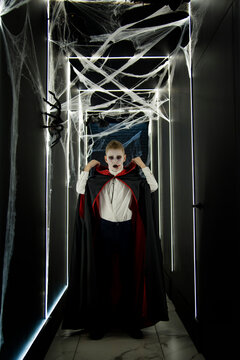  little boy as halloween vampire in red and black hood and black teeth posing in dark studio