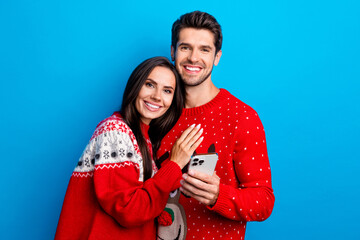 Poster - Photo portrait of pretty young lovers cuddle hold telephone dressed x-mas ornament red sweaters isolated on blue color background