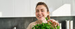 © Mix and Match Studio - Portrait of beautiful smiling girl with bouquet of parsley, standing in the kitchen and cooking, adding herbs to healthy fresh salad or meal, preparing food