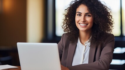 Smiling Adult Indian Woman with Brown Curly Hair Photo. Portrait of Business Person in the office in front of laptop. Photorealistic Ai Generated Horizontal Illustration.