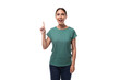 30 year old positive european brunette woman with a ponytail hairstyle is dressed in a green t-shirt and jeans holding her index finger up