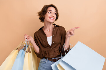 Photo of dreamy pretty girl dressed brown shirt holding bargains looking showing finger empty space isolated beige color background