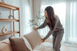 © oatawa - Asian woman arranging pillows on comfortable sofa cushions at home, household, housework and cleaning concept