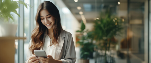 Happy young Asian business woman standing on urban street using cell phone,surfing internet on phone,enjoying morning sunshine outdoor.Modern people.City.