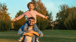 © Belkina Margarita - Laughing little daughter sits on fathers shoulders in autumn park at sunset. Happy family fun walk outdoors. Weekend, leisure, active games
