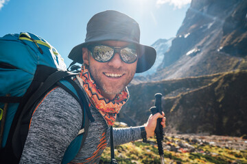 Portrait Young hiker backpacker man in sunglasses smiling at camera in Makalu Barun Park route during high altitude acclimatization walk. Mera peak trekking route, Nepal. Active vacation concept image