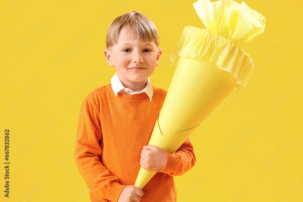 Happy little boy with school cone on yellow background