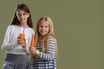 Little girls with glass of juice and carrot on green background