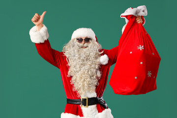 Wall Mural - Cool Santa Claus with bag of gifts showing thumb-up on green background