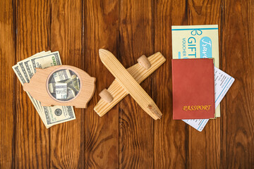 Sticker - Piggy bank with money, toy airplane and travel gift voucher on brown wooden background. Concept of savings for travel