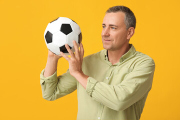 Canvas Print - Handsome mature man playing with soccer ball on yellow background