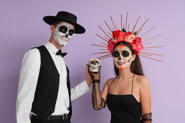 Canvas Print - Young couple dressed for Mexico's Day of the Dead (El Dia de Muertos) with painted skull on lilac background