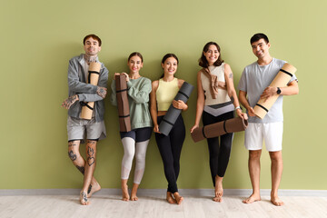 Wall Mural - Group of sporty young people with yoga mats near green wall