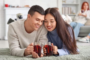 Canvas Print - Happy couple with glasses of warm mulled wine lying on floor in living room at party