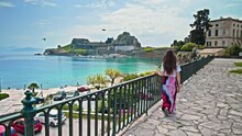 A beautiful woman visiting the Old Fortress of Corfu. Happy girl walks and runs near the scenic ruins of an ancient fort, with artefacts on display, a seating area and a church in Corfu, Greece.
