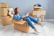 © gorynvd - Happy woman drinks champagne from a glass while sitting inside a cardboard box in new apartment.