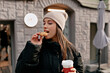 Pretty happy charming woman with dark hair wearing cap is biting cookies and enjoying winter walking outdoor 