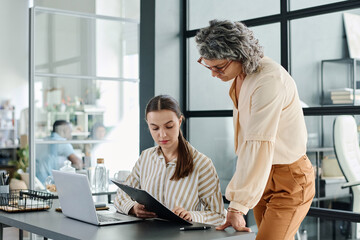 Poster - Young businesswoman with document consulting with her boss about points of contract while preparing it for meeting with partners