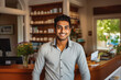 © VisualProduction - Handsome young indian male bed and breakfast owner standing behind counter and smiling, successful business owner at work place