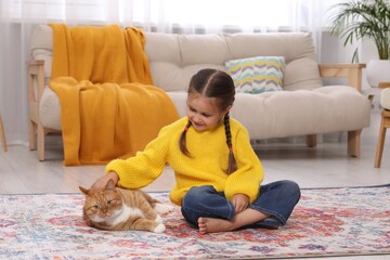 Sticker - Smiling little girl petting cute ginger cat on carpet at home