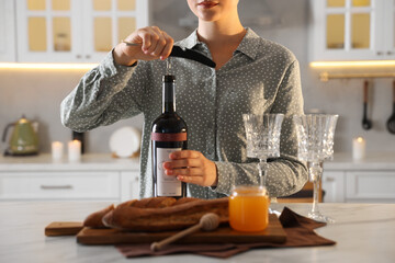 Canvas Print - Romantic dinner. Woman opening wine bottle with corkscrew at table in kitchen, closeup