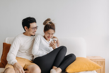 Happy lovely asian couple sharing smartphone to watch together in living room.