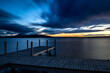 Holzsteg am Seeufers vom Zugersee, Schweiz, bei Abendstimmung, dunklen Wolken und Sonnenuntergang am Horizont