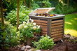 Wooden outdoor composting bin compost bin placed in garden, surrounding flowers and plants. Composting bin to recycle home and garden wastes. Zero waste, sustainable lifestyle