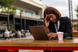 © DusanJelicic - Seated in an urban setting, the businesswoman of color deals with a headache during her coffee break as she checks her agenda for the day.