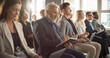 © Gorodenkoff - Senior Caucasian Man Sitting in a Crowded Audience at a Business Forum. Corporate Delegate Taking Notes. Successful Male CEO Attending Business Conference, Listening To Presentation.