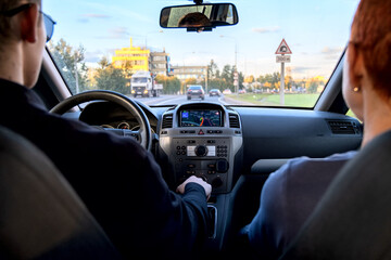 Blurry view of the road through the windshield of the car. The car control panel, the navigator is turned on. The driver and passenger are looking forward.