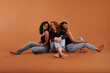 © Flamingo Images - Stylish young women laughing while sitting on an orange background