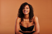 Young black woman wearing a strapless bra smiling on an orange background
