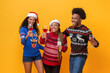 Happy diverse friends in Christmas sweaters drinking, singing, celebrating and having fun together in yellow isolated background studio shot