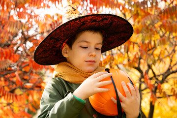 Happy Halloween child holding a pumpkin candy bucket while standing in the autumn forest